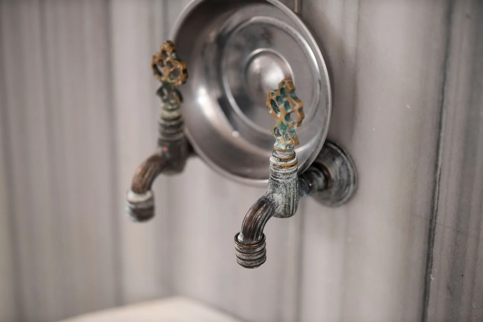 A row of ornate metal faucets mounted on a tiled wall