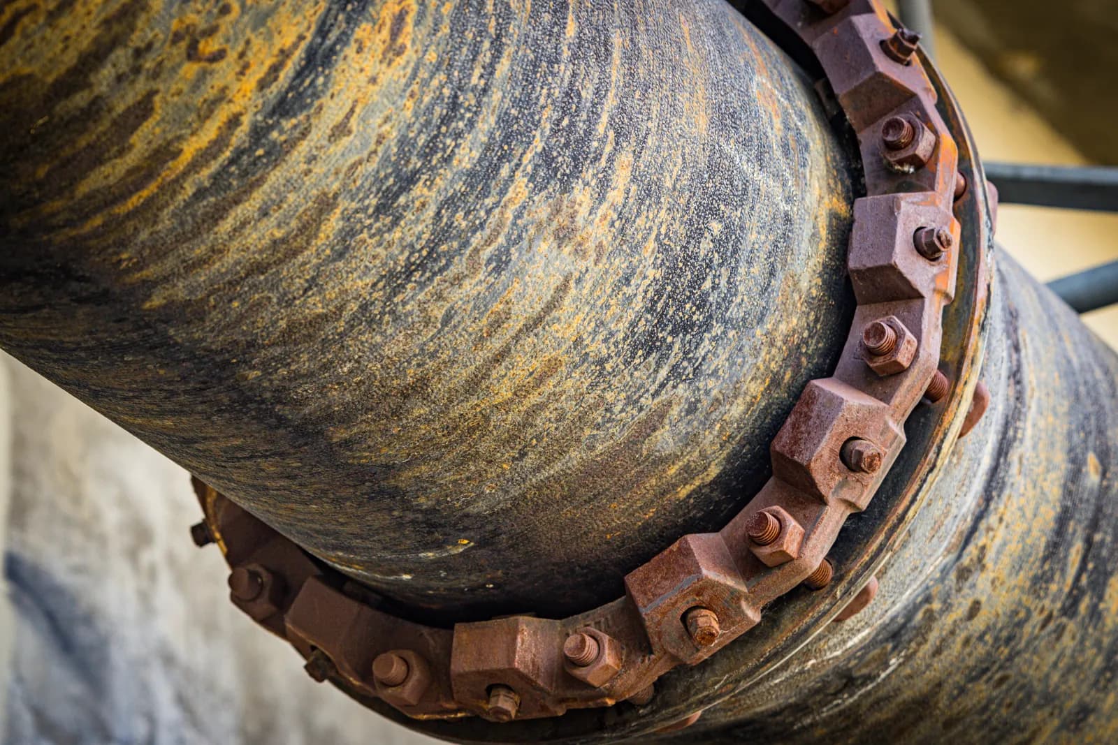 A close-up of a large rusted iron pipe with bolted flanges