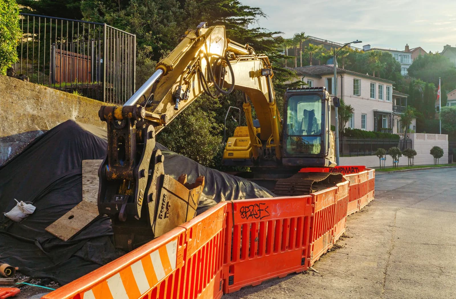An excavator and orange barricades at a residential street dig