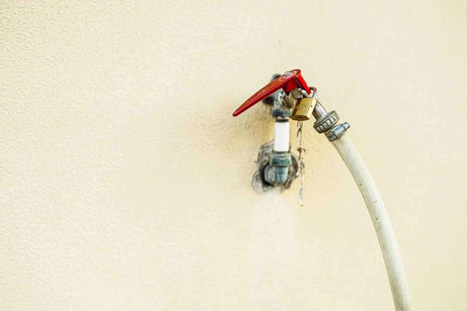 An outdoor wall-mounted water faucet with a bright red handle