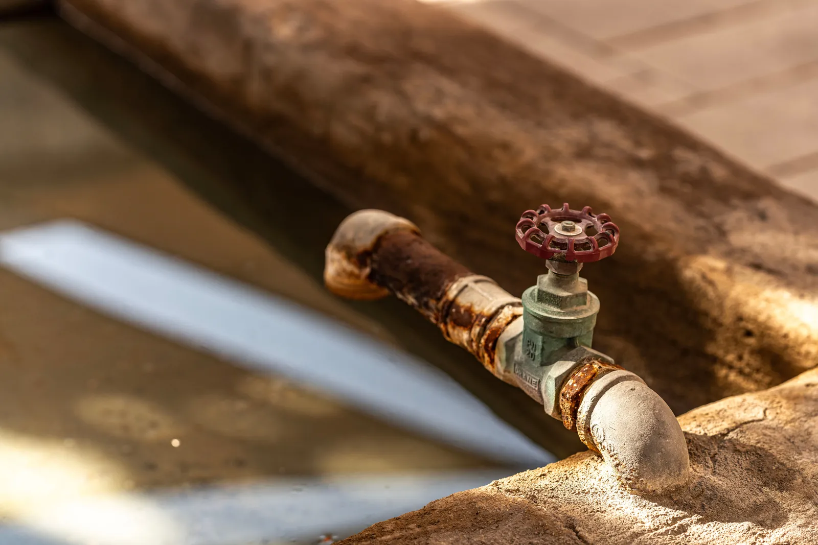 A red-handled gate valve on a corroded galvanized water line