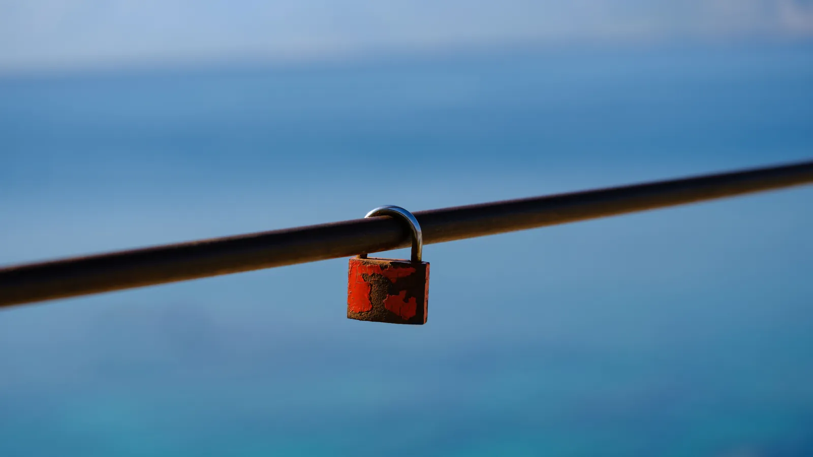 A heavily rusted padlock on a metal rail with the sea behind it