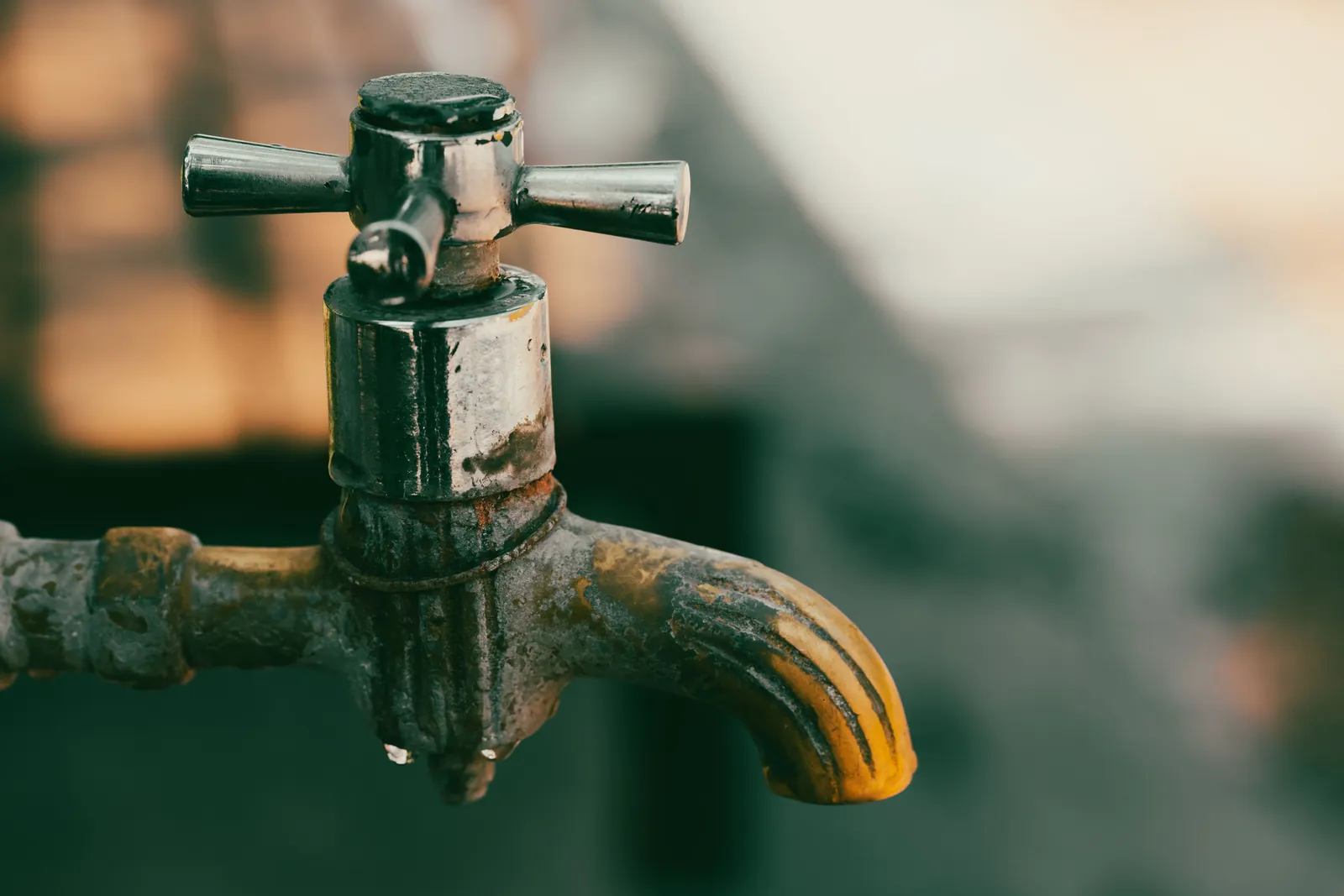 Close-up of a weathered metal faucet with water beading on the spout