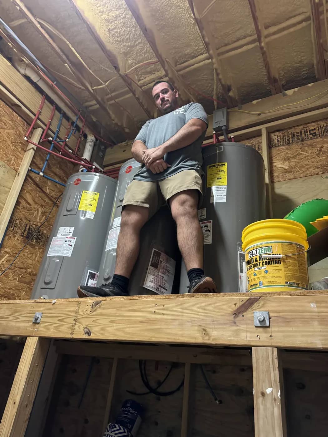 Multi-unit water heater installation Streamlined Plumbing technician beside three tank water heaters in a framed mechanical room.