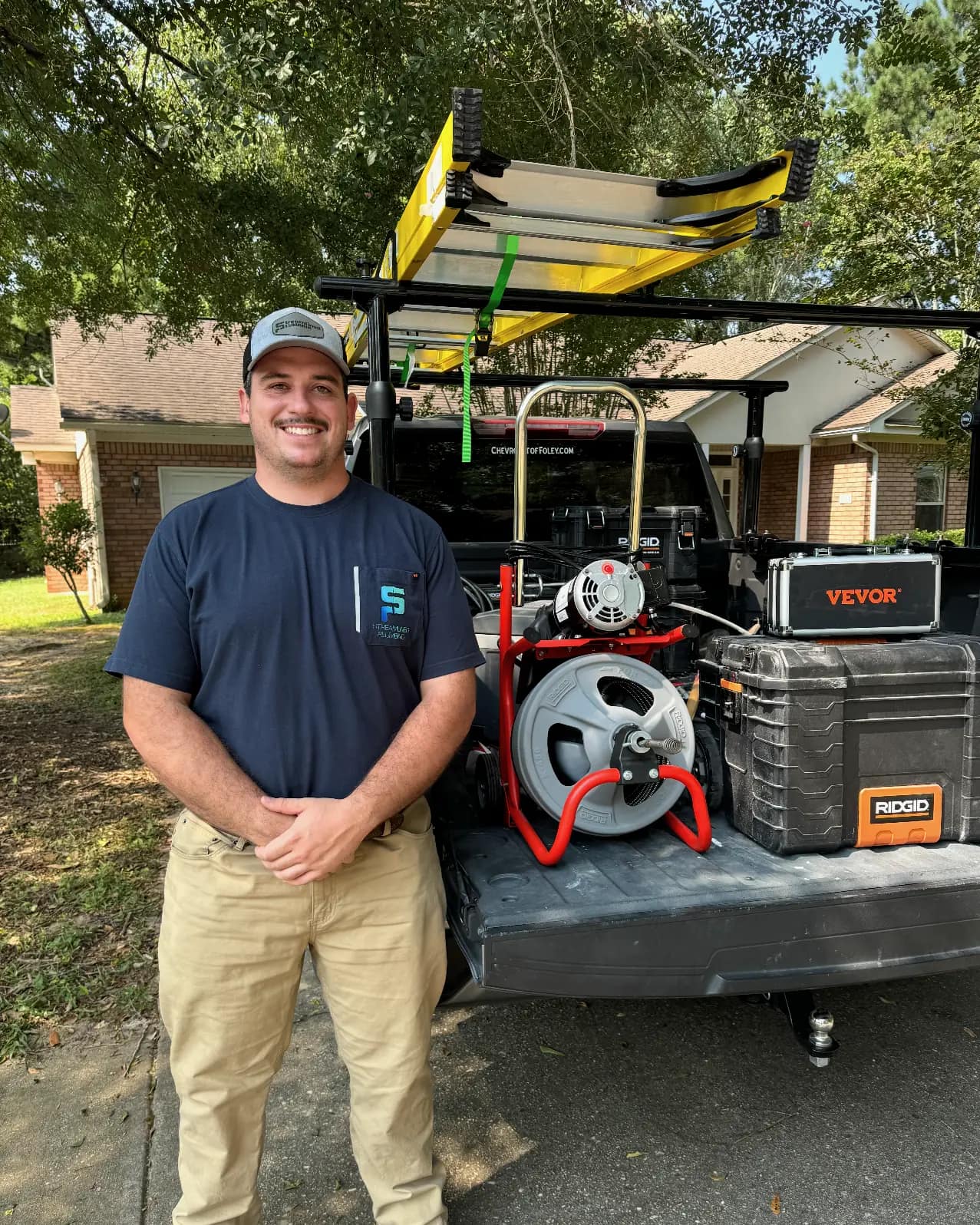 Brandon Byrd, owner and Alabama Master Plumber Brandon Byrd in a Streamlined Plumbing shirt and cap, standing beside his work truck loaded with a drum drain machine, tool cases and a ladder rack.