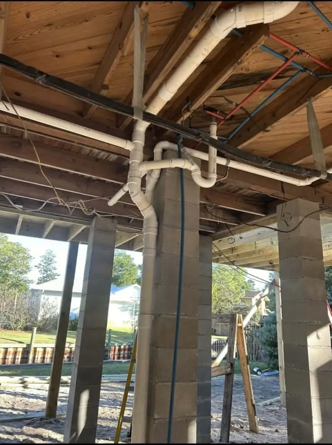 Exposed drain piping beneath a raised coastal home during plumbing work.